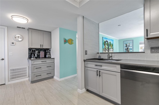 kitchen with sink, light hardwood / wood-style flooring, stainless steel dishwasher, backsplash, and gray cabinetry