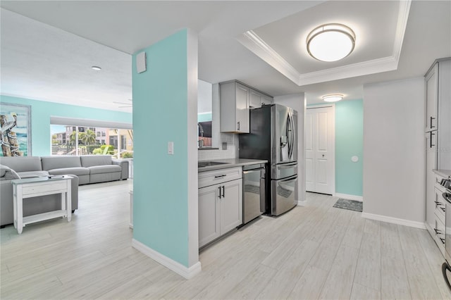 kitchen with stainless steel appliances, a raised ceiling, light hardwood / wood-style floors, decorative backsplash, and crown molding