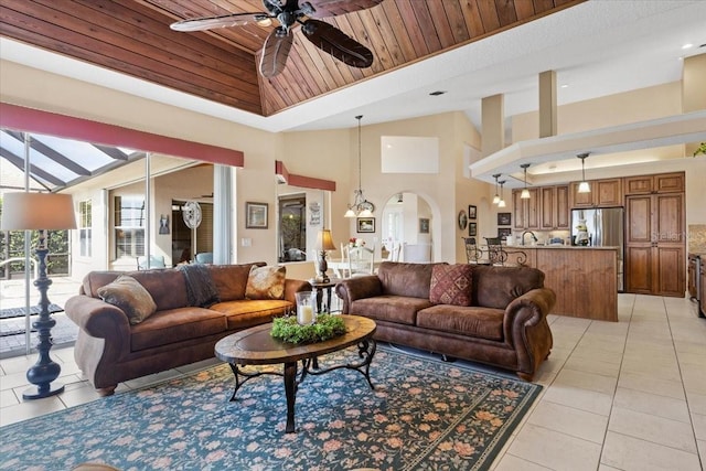 living room featuring wood ceiling, ceiling fan with notable chandelier, light tile patterned floors, and a towering ceiling