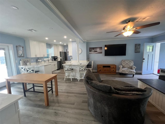 living room featuring light wood-type flooring, ceiling fan, crown molding, and sink