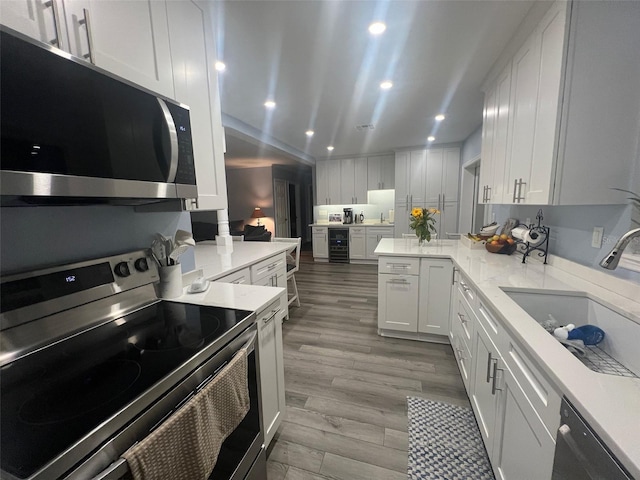 kitchen featuring white cabinetry, sink, wine cooler, kitchen peninsula, and appliances with stainless steel finishes