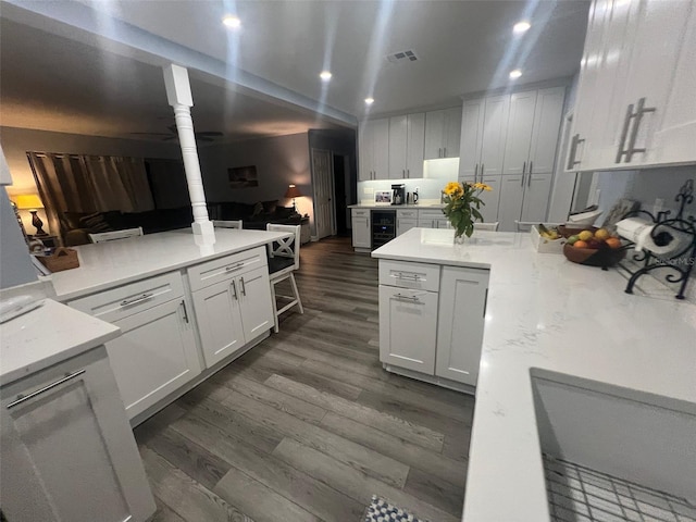 kitchen with wine cooler, light stone counters, white cabinets, and dark wood-type flooring