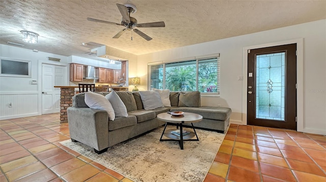 living room featuring a textured ceiling, light tile patterned floors, wainscoting, and a ceiling fan