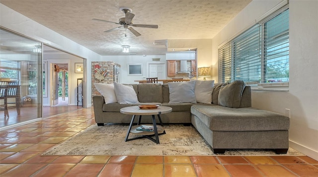 living room with tile patterned flooring, ceiling fan, a textured ceiling, and baseboards