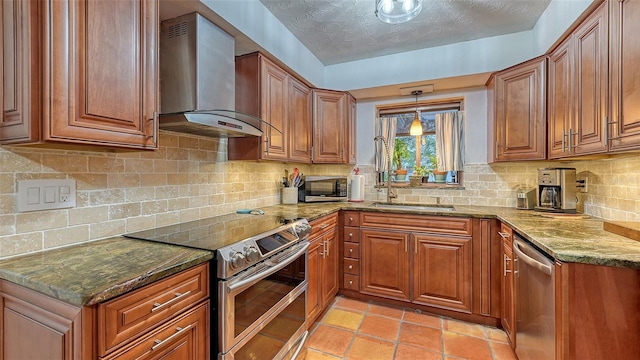 kitchen featuring brown cabinets, stainless steel appliances, a sink, wall chimney range hood, and dark stone countertops