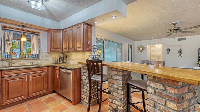 kitchen with visible vents, backsplash, brown cabinetry, a sink, and dishwasher