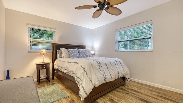 bedroom with a ceiling fan, multiple windows, baseboards, and wood finished floors