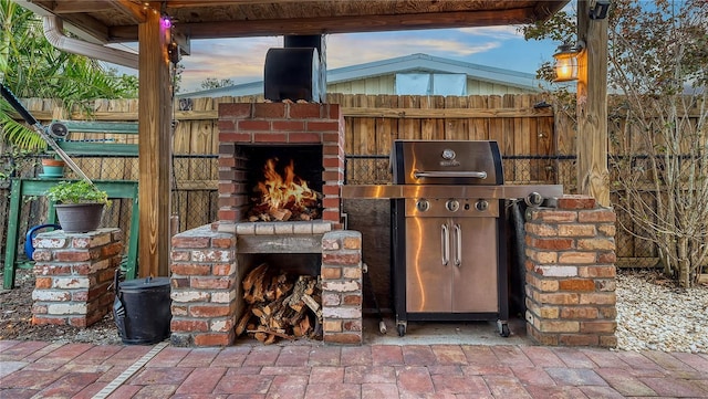 view of patio / terrace with an outdoor brick fireplace, fence, and grilling area