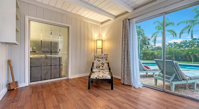 sitting room with wood walls, baseboards, beam ceiling, and wood finished floors