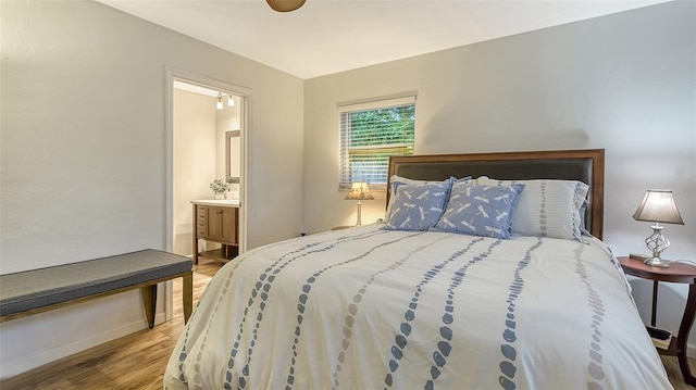 bedroom with light wood-style floors, ensuite bath, and baseboards