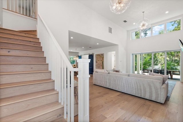 living room featuring a chandelier, a high ceiling, a barn door, and light hardwood / wood-style flooring