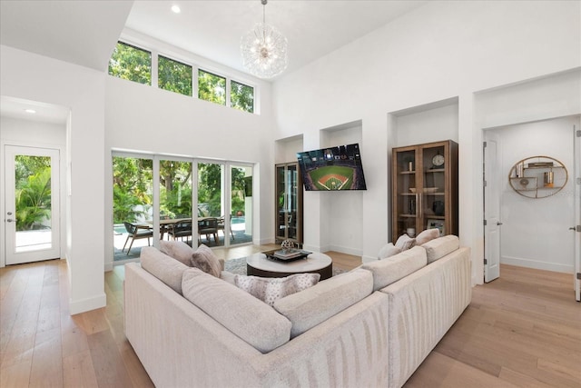 living room with light hardwood / wood-style floors, a high ceiling, a wealth of natural light, and an inviting chandelier