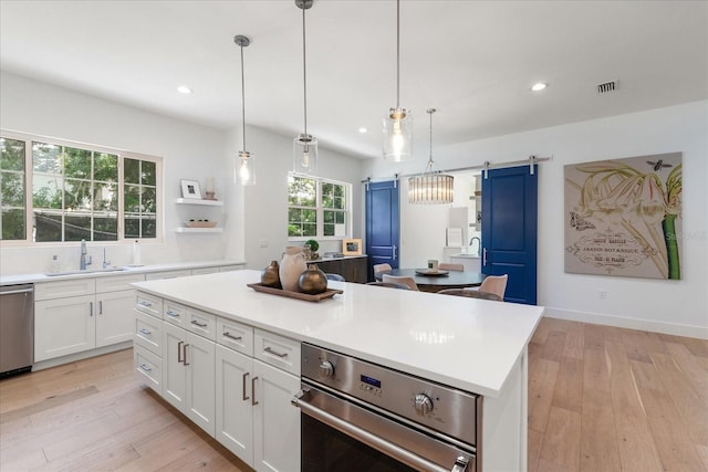 kitchen featuring sink, hanging light fixtures, a kitchen island, a barn door, and white cabinets