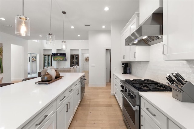 kitchen with wall chimney exhaust hood, stainless steel appliances, pendant lighting, light hardwood / wood-style flooring, and white cabinets