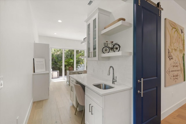 kitchen with a barn door, white cabinetry, sink, and decorative backsplash