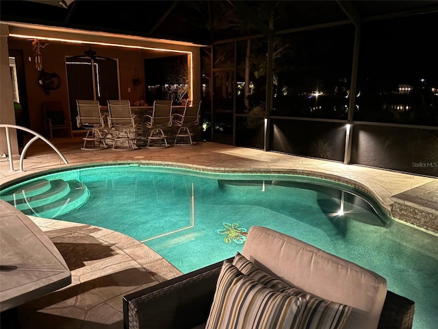 pool at night with ceiling fan, a lanai, and a patio area