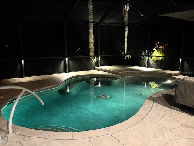 pool at twilight with glass enclosure and a patio area