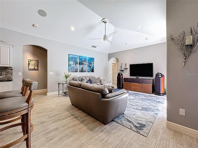 living room featuring light wood-type flooring, arched walkways, baseboards, and ceiling fan