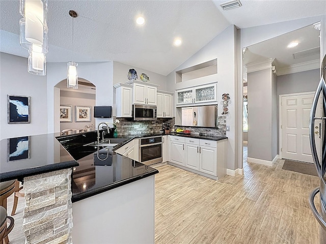 kitchen with a peninsula, dark countertops, appliances with stainless steel finishes, and a sink