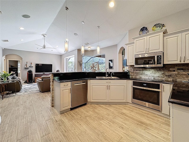 kitchen with a peninsula, lofted ceiling, arched walkways, a sink, and appliances with stainless steel finishes