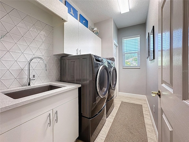 clothes washing area featuring baseboards, a textured ceiling, separate washer and dryer, a sink, and cabinet space