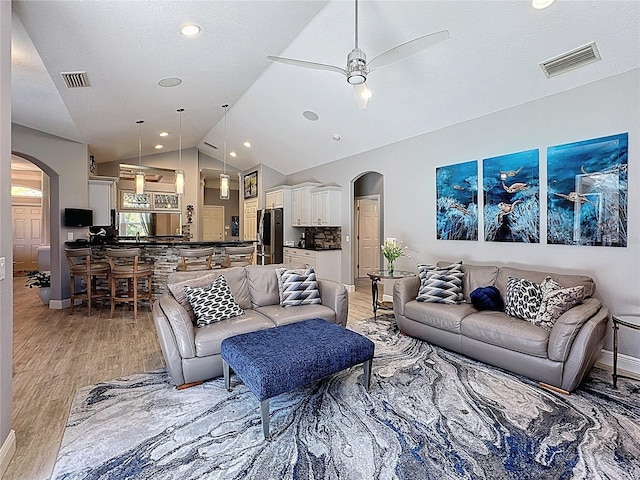 living room featuring visible vents, arched walkways, lofted ceiling, and light wood-type flooring