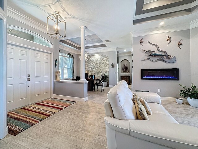 foyer entrance featuring crown molding, decorative columns, a glass covered fireplace, and an inviting chandelier