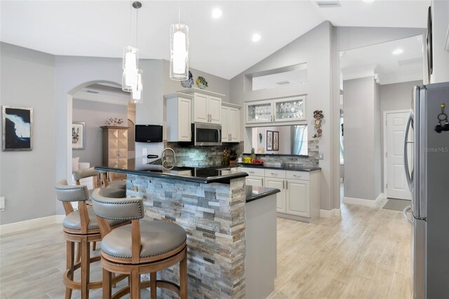 kitchen featuring dark countertops, arched walkways, a breakfast bar, stainless steel appliances, and light wood-style flooring