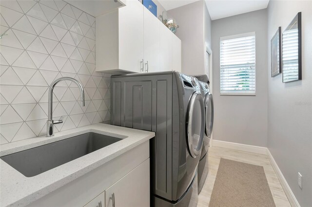 clothes washing area featuring cabinet space, separate washer and dryer, baseboards, and a sink