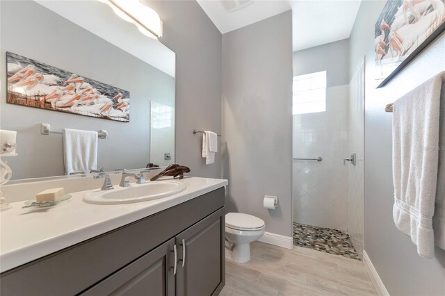 bathroom featuring wood finished floors, a walk in shower, baseboards, vanity, and toilet