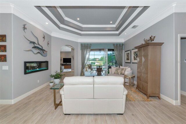 living room with crown molding, a raised ceiling, light wood-type flooring, and visible vents