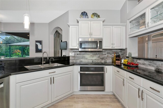 kitchen featuring backsplash, appliances with stainless steel finishes, dark countertops, a sink, and white cabinetry