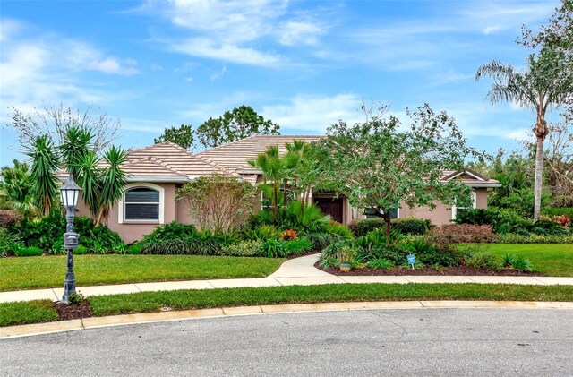 ranch-style house featuring a tile roof, a front yard, and stucco siding