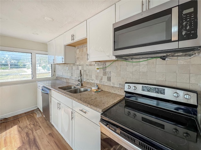 kitchen with sink, light hardwood / wood-style flooring, light stone countertops, appliances with stainless steel finishes, and white cabinetry