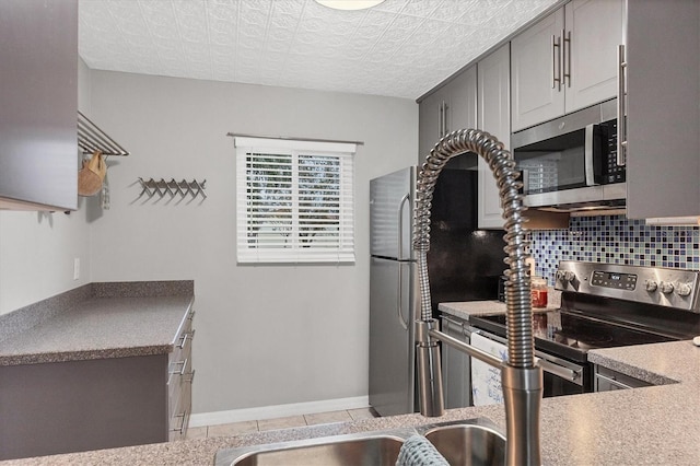 kitchen with stainless steel appliances, gray cabinetry, backsplash, and a textured ceiling