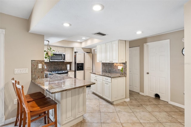 kitchen with stone counters, a breakfast bar area, stove, paneled built in fridge, and kitchen peninsula