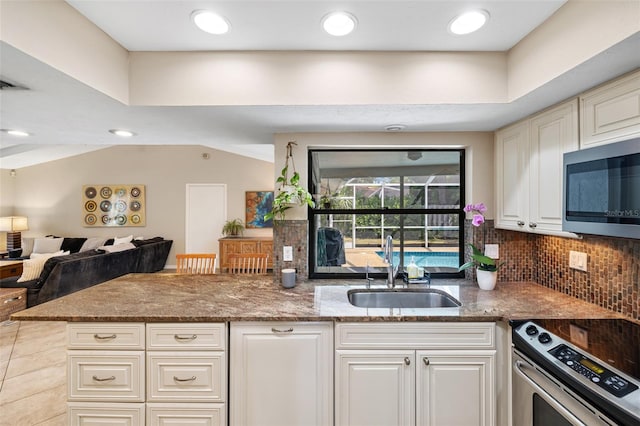 kitchen with sink, dark stone countertops, appliances with stainless steel finishes, kitchen peninsula, and white cabinets