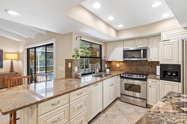 kitchen featuring sink, appliances with stainless steel finishes, light stone counters, a kitchen bar, and kitchen peninsula