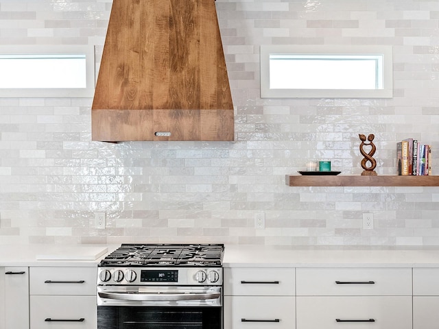 kitchen featuring gas range, white cabinetry, tasteful backsplash, and wall chimney range hood