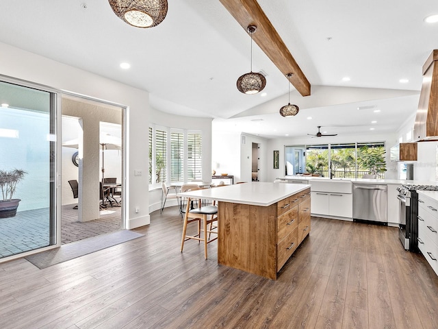 kitchen featuring pendant lighting, appliances with stainless steel finishes, white cabinetry, hardwood / wood-style floors, and a center island