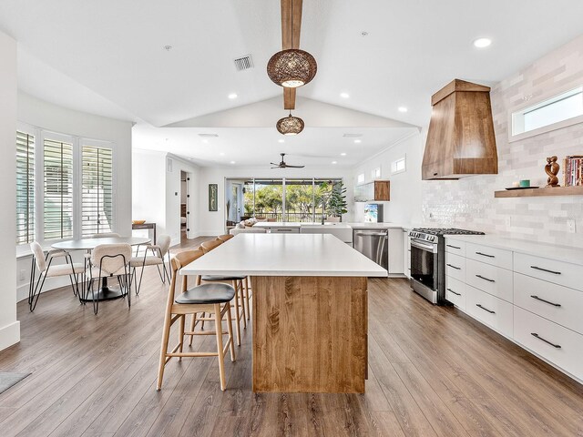 kitchen with appliances with stainless steel finishes, white cabinets, a kitchen island, decorative backsplash, and light wood-type flooring