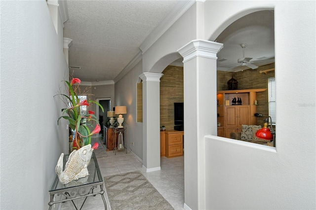 corridor with light tile patterned flooring, ornamental molding, a textured ceiling, and decorative columns