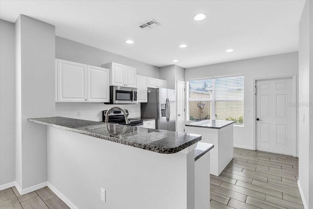 kitchen featuring stainless steel appliances, kitchen peninsula, dark stone countertops, a breakfast bar, and white cabinets