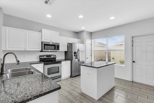 kitchen with appliances with stainless steel finishes, dark stone counters, sink, white cabinets, and a center island