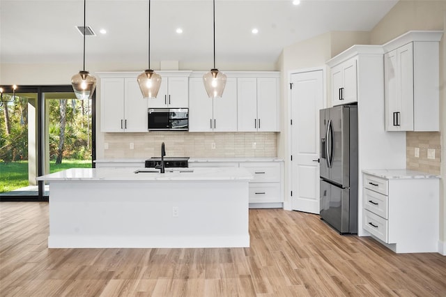 kitchen with a kitchen island with sink, appliances with stainless steel finishes, hanging light fixtures, light stone counters, and white cabinetry