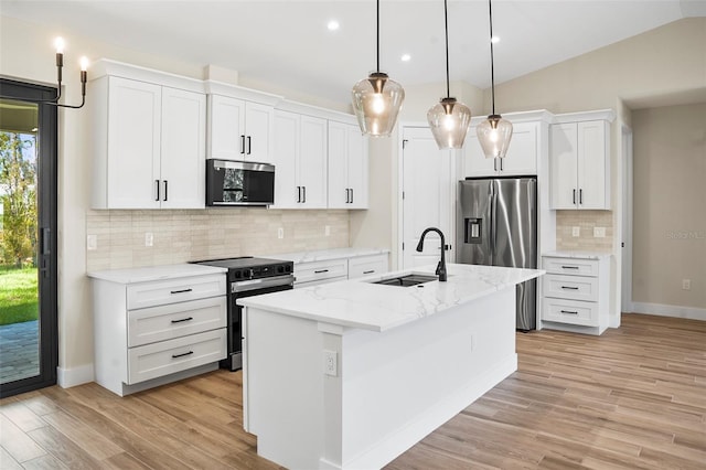 kitchen with vaulted ceiling, a center island with sink, stainless steel appliances, pendant lighting, and white cabinets