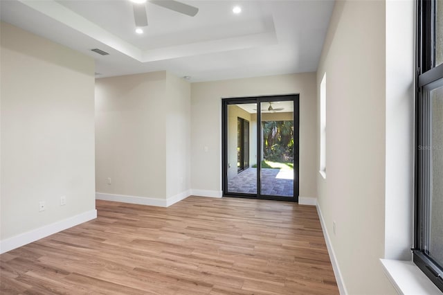 empty room featuring ceiling fan, a tray ceiling, and light hardwood / wood-style flooring