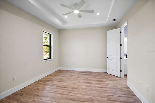 unfurnished room with a raised ceiling, light wood-type flooring, and ceiling fan