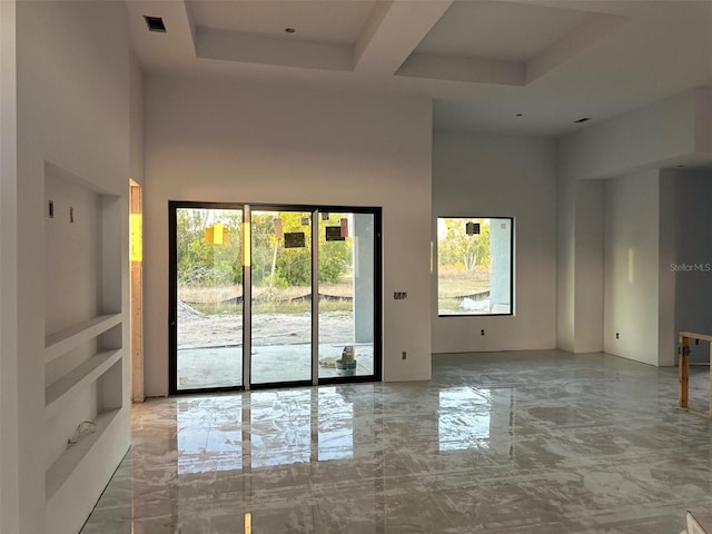 spare room featuring a towering ceiling, built in features, and a raised ceiling