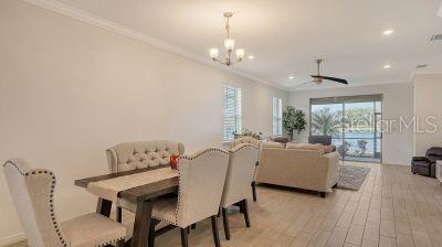 dining area with light wood-type flooring, ceiling fan with notable chandelier, and crown molding